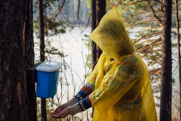 Mujer desconocida en impermeable amarillo se lava las manos en el lavabo colgando de un árbol.