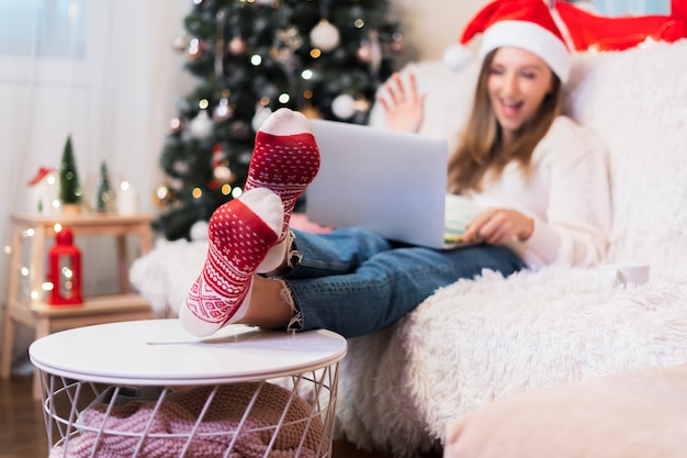 Mujer desenfocada en calcetines rojos con un chat de videollamada en la computadora portátil, disfrute de la Navidad en casa