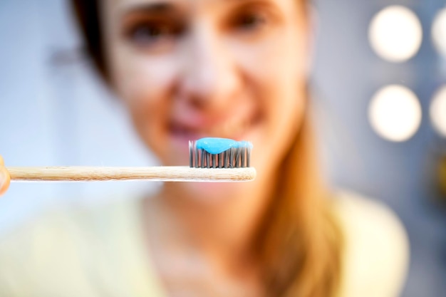 Mujer desenfocada en el fondo sonriendo sosteniendo un cepillo de dientes de bambú con higiene de pasta de dientes y concepto de limpieza diaria de dientes