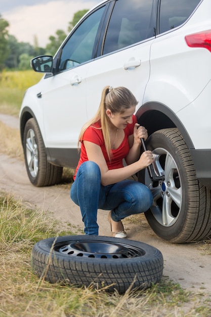 Foto mujer desenroscando las tuercas de la rueda plana del coche en el campo