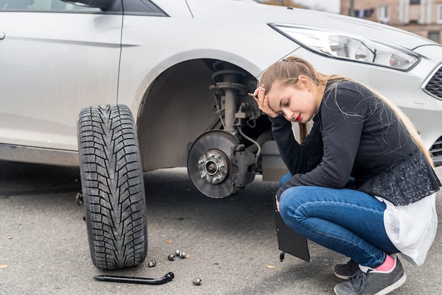 Mujer desesperada mirando rueda de repuesto para coche