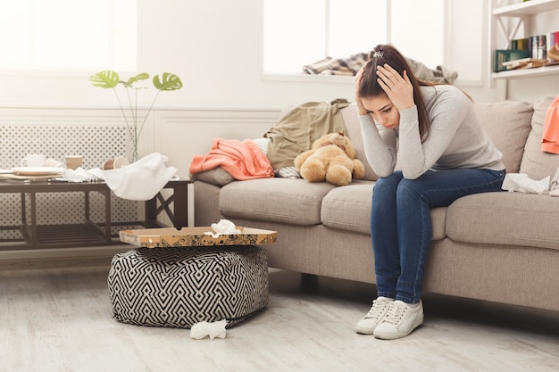 Mujer desesperada sentada en el sofá en la habitación desordenada