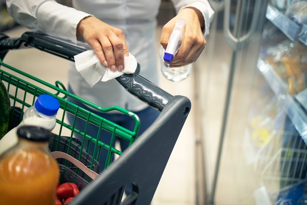 Mujer desinfectando el carrito de compras con desinfectante antes de usarlo debido a la pandemia del virus corona.