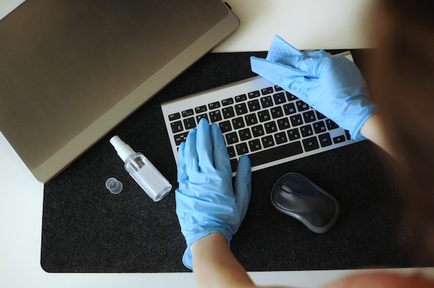 Mujer desinfectando dispositivos en el lugar de trabajo. Prevención de la propagación de virus desinfectando el teclado