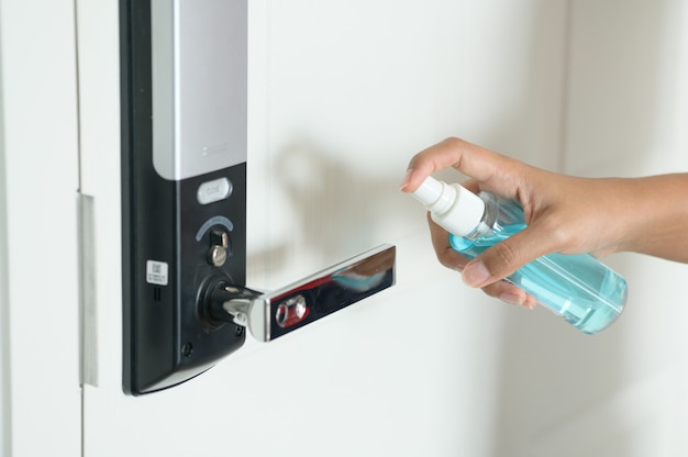 Mujer desinfectando el pomo de la puerta rociando un desinfectante azul de una botella, Prevent covid19, corona virus.