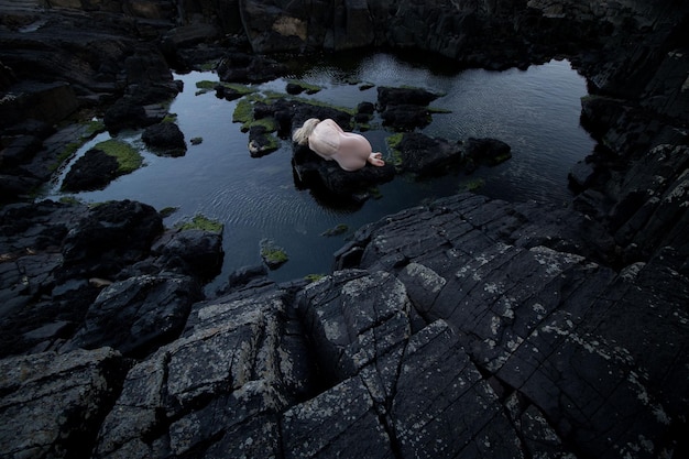 Mujer desnuda en la roca por el lago contra el cielo