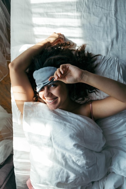 Mujer despertando en la máscara para dormir de la mañana brillante