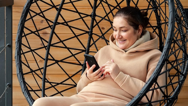 Mujer desplaza el teléfono inteligente con una sonrisa sentada en la terraza