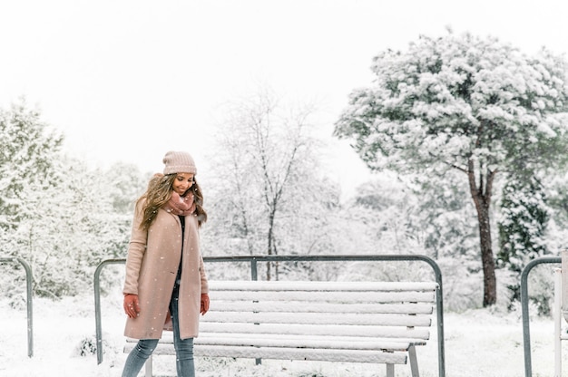 Mujer despreocupada en ropa de abrigo dando la vuelta con los brazos extendidos mientras disfruta de un día de nieve en invierno en el parque