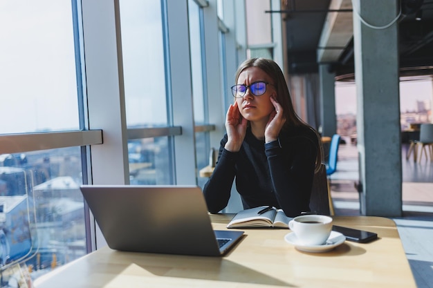 Una mujer después de un duro día de trabajo se sienta en una computadora portátil y se aferra a su cabeza