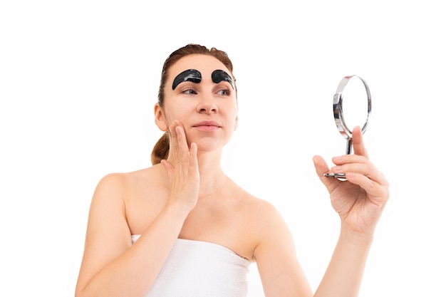 Mujer después de procedimientos cosméticos mira en un pequeño espejo sobre un fondo blanco cosmético negro