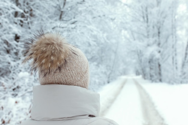 Mujer por detrás caminando por un camino arbolado blanco nevado en un bosque en invierno vertical