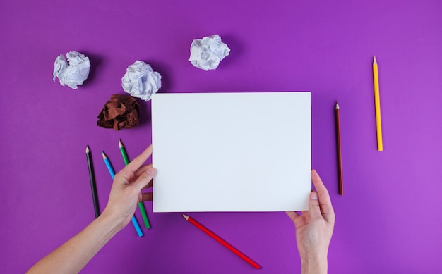 Mujer va a dibujar con lápices de colores sobre una superficie morada con bolas de papel arrugado.