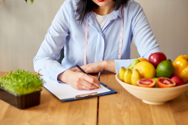 Mujer dietista escribiendo un plan de dieta, con frutas y verduras saludables