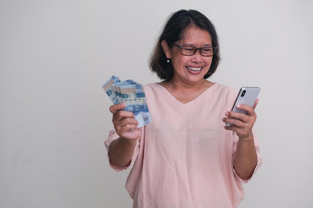 Una mujer con dinero en una mano y un teléfono inteligente en la otra sonriendo