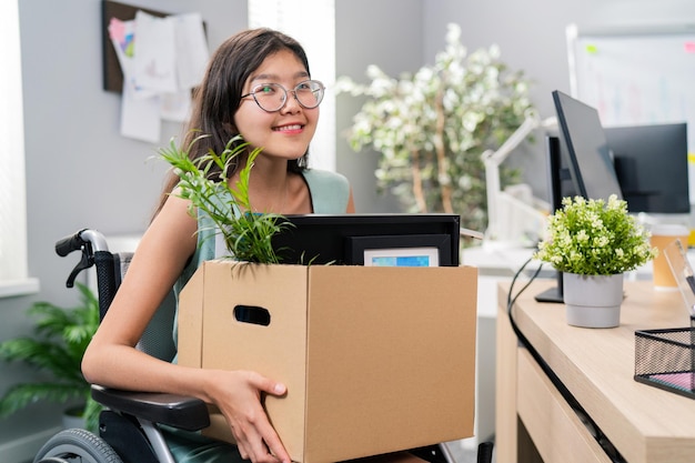 Mujer con discapacidad con anteojos y belleza coreana asiática se sienta en silla de ruedas en el escritorio corporativo