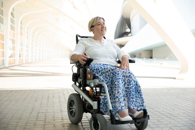Una mujer discapacitada elegante y sonriente sentada en una silla de ruedas disfrutando del paseo por la ciudad