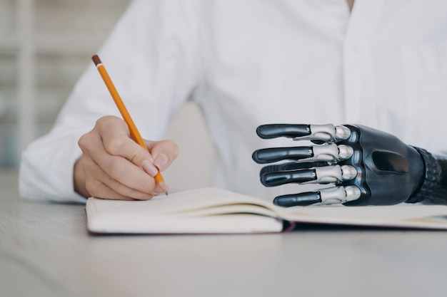 Mujer discapacitada escribiendo con lápiz en un cuaderno usando un brazo protésico biónico closeup Tecnología médica