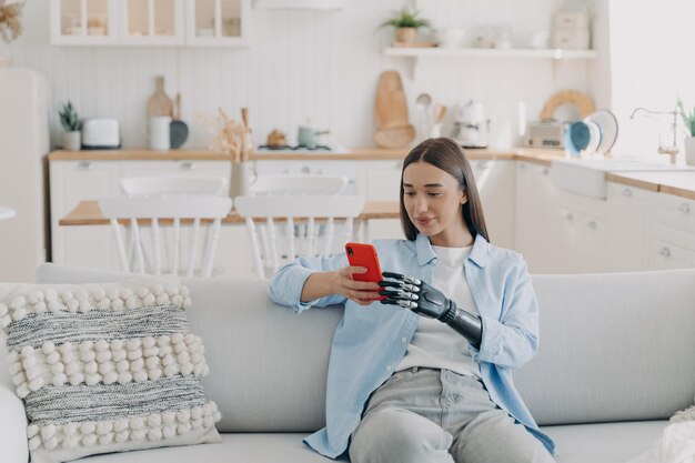 Mujer discapacitada está enviando mensajes de texto en el teléfono inteligente Niña feliz sosteniendo el teléfono con brazo artificial biónico