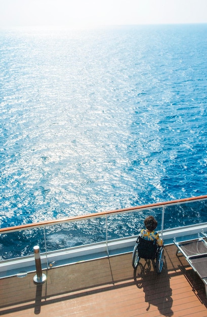 Mujer discapacitada en silla de ruedas en la cubierta de un crucero mirando la brillante luz del sol el concepto de accesibilidad de viaje para discapacitados