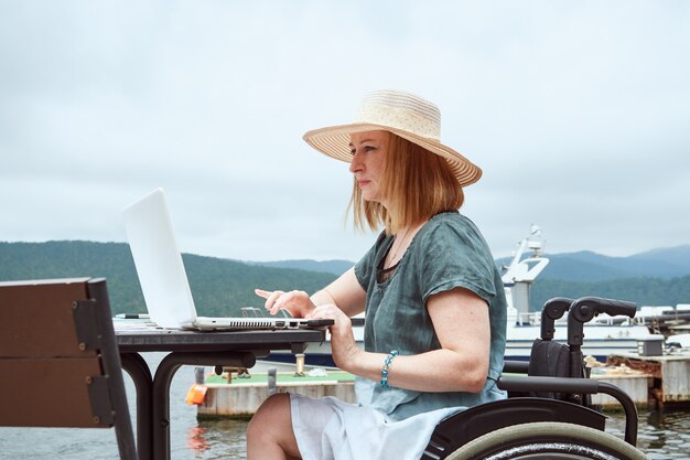 Mujer discapacitada usa laptop al aire libre. Trabajo remoto, concepto de aprendizaje.