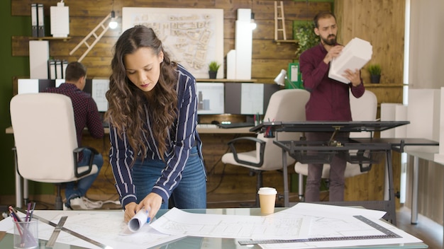 Mujer diseñadora en la agencia de medios creativos lookign en planos en la oficina moderna