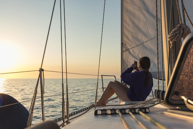 Mujer disfrutando de una colorida puesta de sol en un velero navegando en el mar