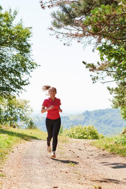 mujer disfrutando de un estilo de vida saludable mientras trota en una carretera rural a través del hermoso bosque soleado, el ejercicio y el concepto de fitness