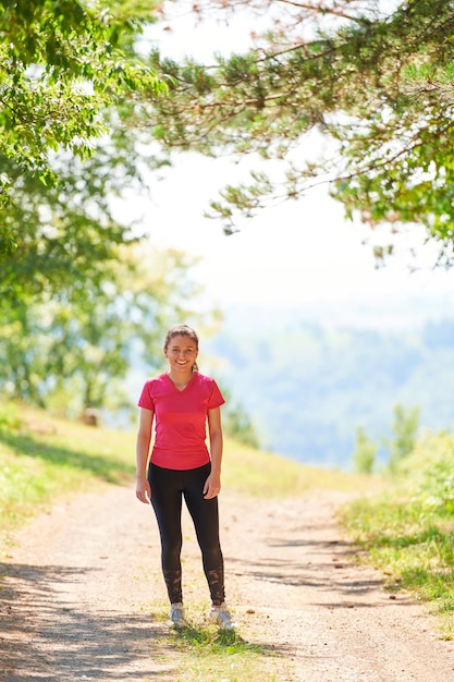 mujer disfrutando de un estilo de vida saludable mientras trota en una carretera rural a través del hermoso bosque soleado, el ejercicio y el concepto de fitness