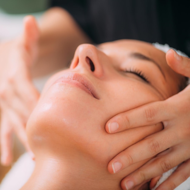 Foto mujer disfrutando de un masaje facial ayurvédico profesional con aceites esenciales terapéuticos