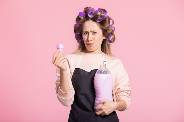 La mujer disgustada sostiene el detergente para la ropa en las manos con la tapa del olor desagradable del detergente La niña se para contra un fondo de estudio rosa