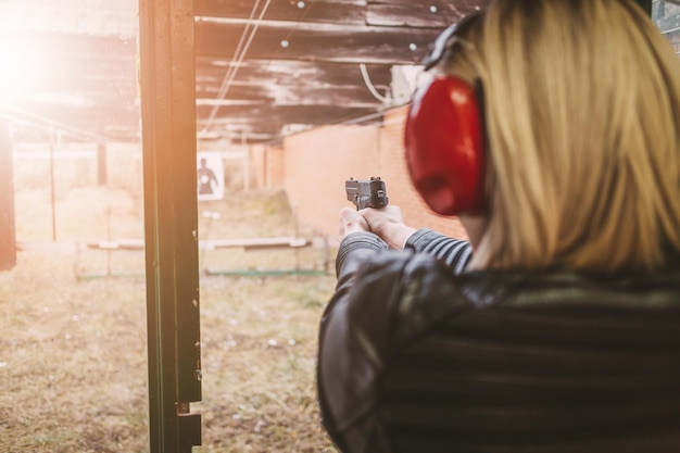 Foto mujer disparando con pistola al blanco en el campo de tiro. vista trasera.