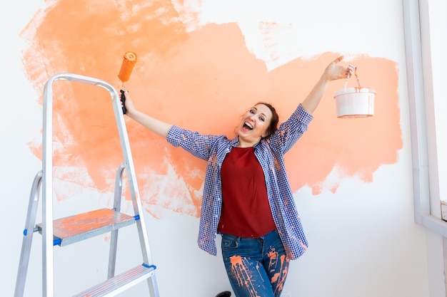 Mujer divertida pintando la pared con rodillo de pintura.