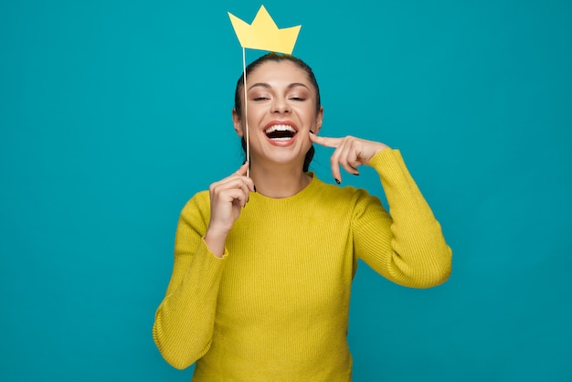 Mujer divertida que presenta con la corona de papel sobre fondo azul