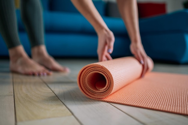 Mujer doblando colchoneta rosa mientras practica yoga en casa