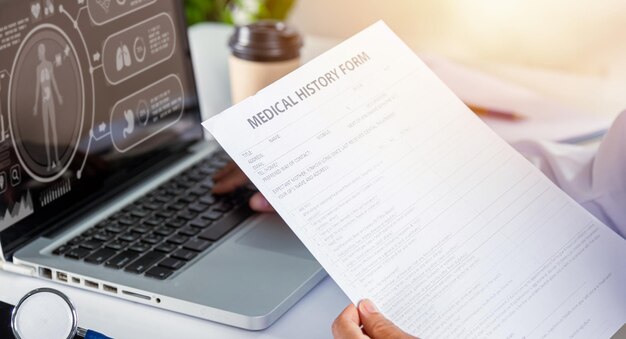 Mujer doctora escribiendo información de la prescripción del paciente del formulario de historial médico en papeleo en la computadora portátil