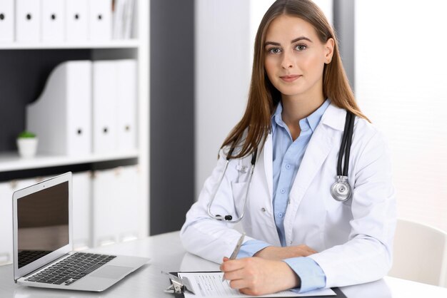 Mujer doctora llenando formularios médicos mientras está sentada en el escritorio de la oficina del hospital. Médico en el trabajo. Concepto de medicina y atención de la salud.