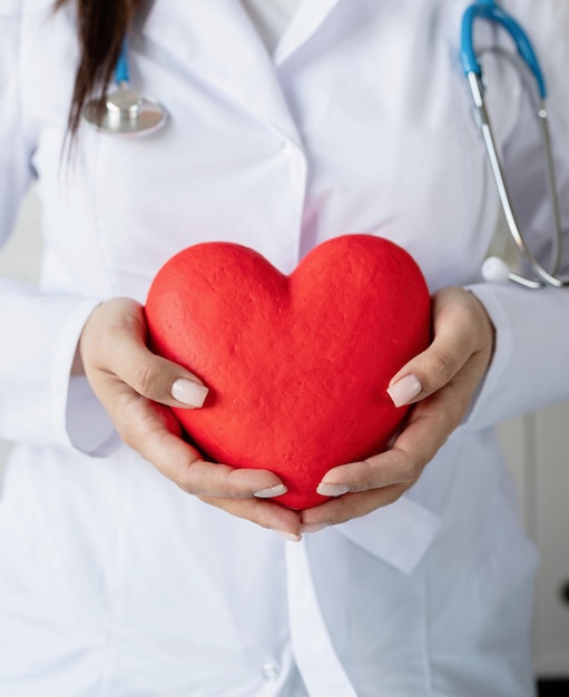 Mujer doctora o científica sosteniendo un gran corazón rojo en las manos