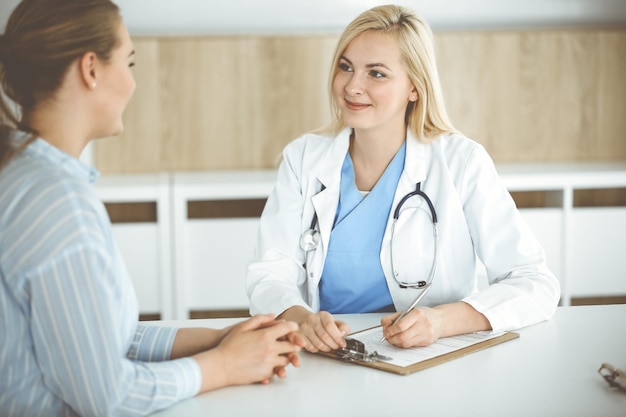 Mujer doctora y paciente sentada y hablando en el hospital o clínica Terapeuta rubia