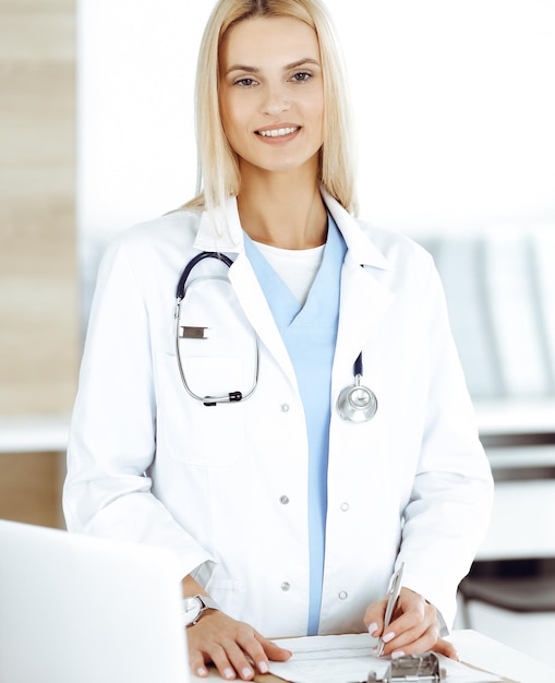 Mujer doctora en el trabajo en la clínica feliz de su profesión La doctora rubia controla el registro del historial de medicamentos y los resultados del examen médico Concepto de medicina