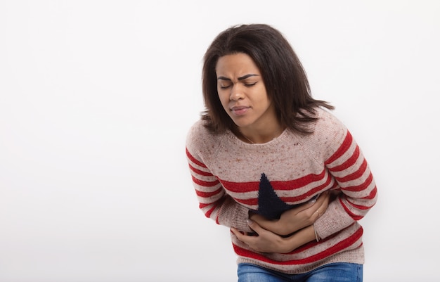 Mujer con dolor de abdomen de estómago que tiene malos dolores aislados en la pared blanca. expresión facial