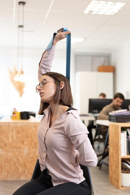 Mujer con dolor de espalda estirando y relajando su espalda con una banda elástica de pilates en la oficina