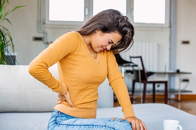 Foto mujer con dolor de espalda sentada en el sofá