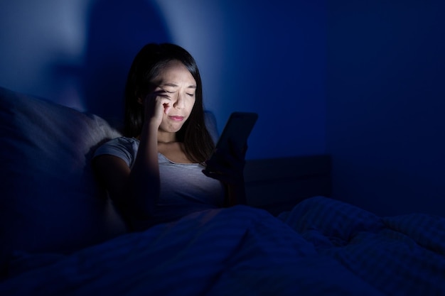 Mujer con dolor en el ojo por usar el teléfono móvil por la noche