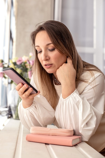 Mujer doméstica agradable que se relaja en la cocina moderna charlando utiliza el interior de la cocina blanca del smartphone