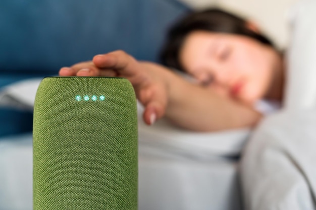 Una mujer dormida apagando el despertador en un altavoz inalámbrico portátil
