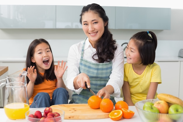 Mujer con dos hijas alegres cortar fruta en la cocina