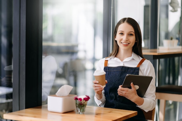 Mujer dueña de una cafetería sosteniendo un bloc de notas y una tableta digital lista para recibir pedidos en un café restaurante mujer barista café xA