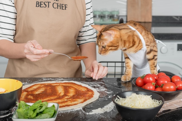 La mujer dueña y su gato colocan las coberturas de la pizza en la masa