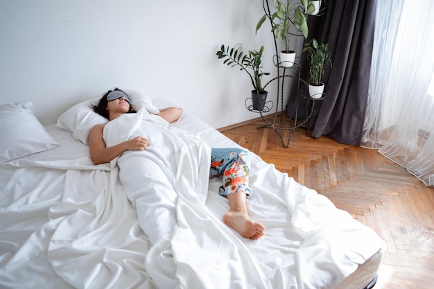 Mujer durmiendo con antifaz para dormir en la cama con sábanas blancas